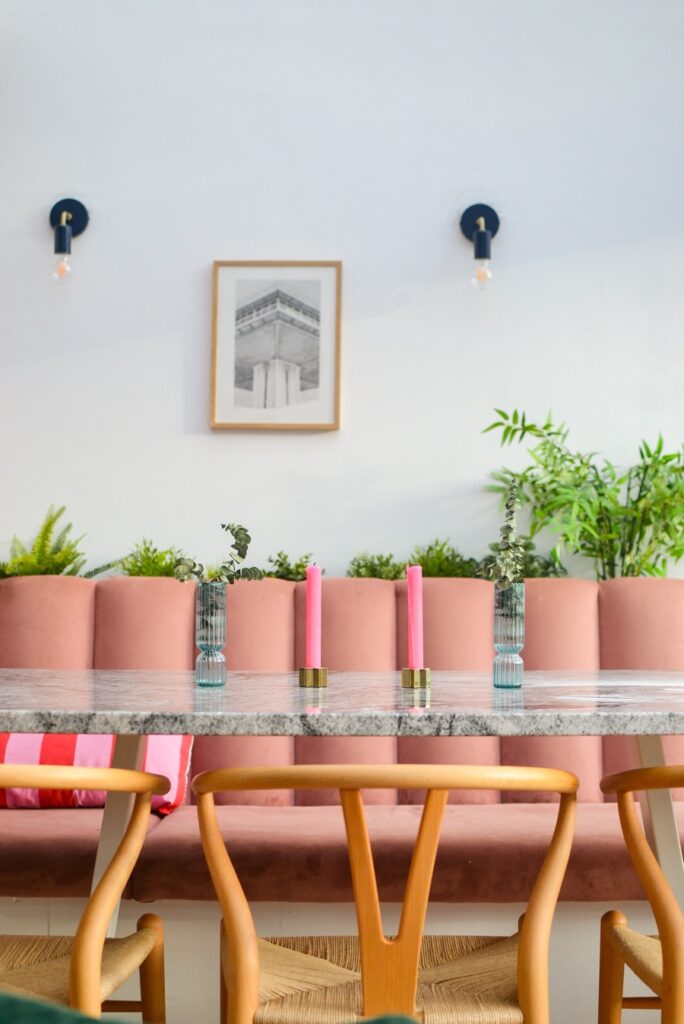 Pink velvet bench seating dining area with marble table and bright pink candles. Carl Hansen Wishbone chairs.
